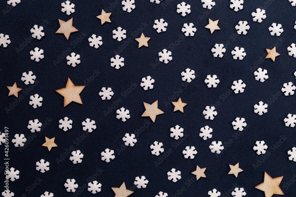 Small white snowflakes and wooden stars on a dark acrylic background taken close up Small white snowflakes and wooden stars on a dark acrylic background taken close up