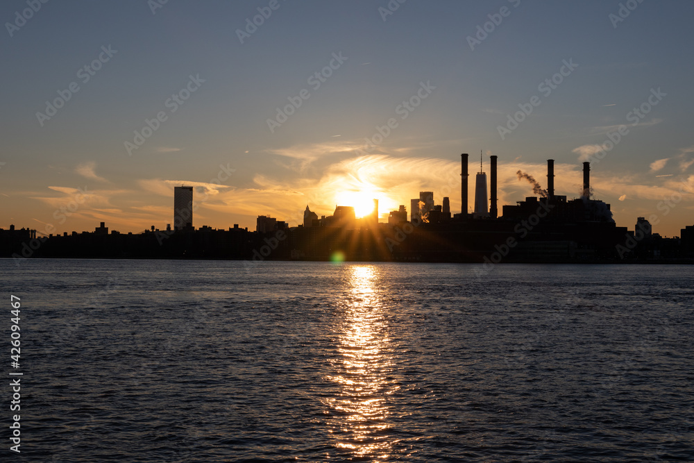 Naklejka premium Bright Sunset and the Manhattan Skyline Silhouette with Smoke Stacks along the East River in New York City