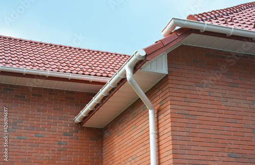 Tableau sur toile A close-up on plastic rain gutters, downspout, soffit and fascia with a box-end on the corner of a brick house as important parts of roofing system waterproofing and ventilation