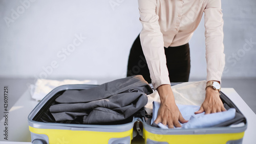 cropped view of businesswoman packing clothes in baggage at home