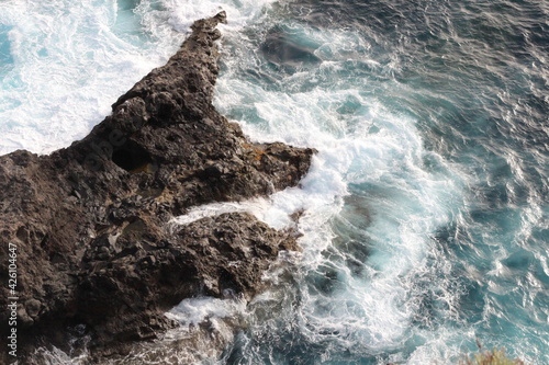 Turquoise ocean waves crashing against the rocks. Bird's eye view of the ocean water, from above.
