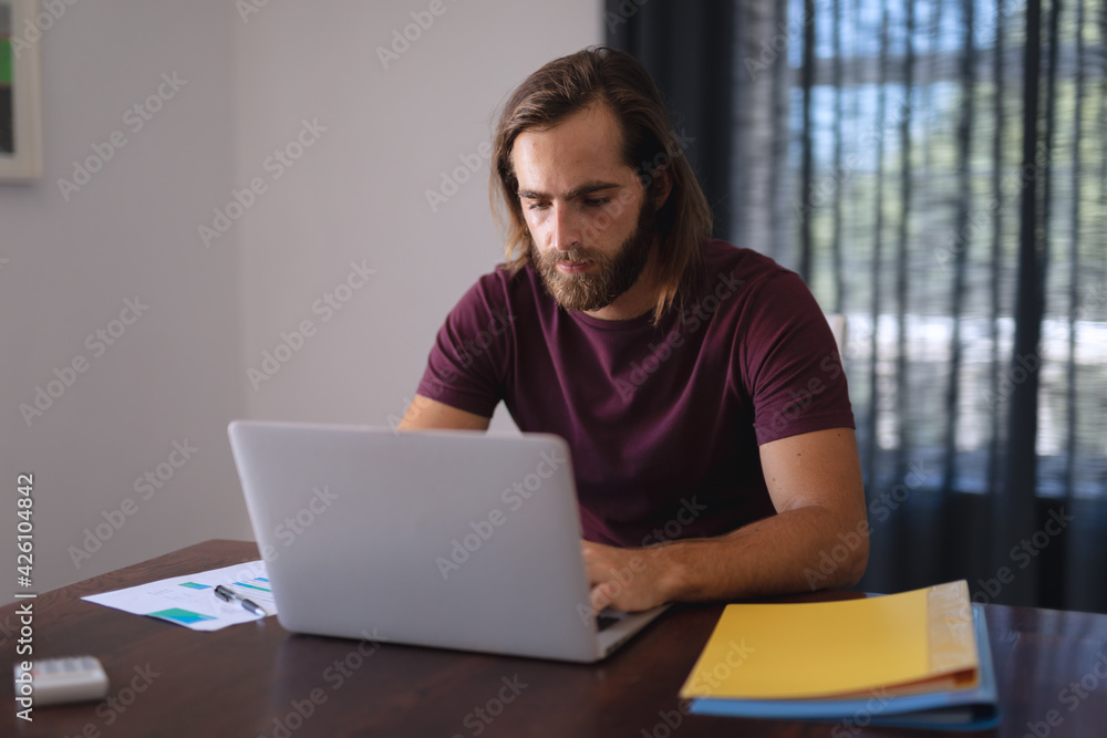 Caucasian man sitting at table working from home and using laptop Caucasian man sitting at table working from home and using laptop