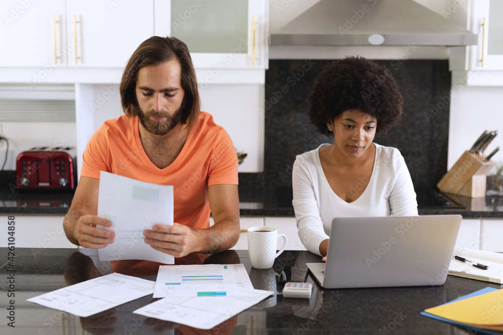Diverse couple sitting in kitchen using laptop and paying bills Diverse couple sitting in kitchen using laptop and paying bills