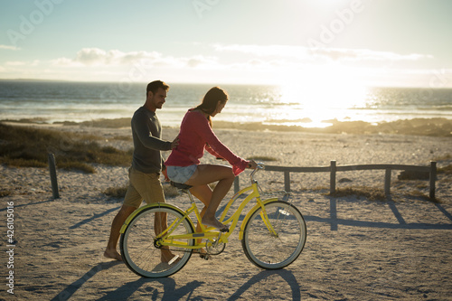 Happy caucasian couple at the sea learning to ride bicycle