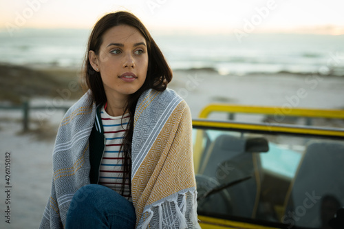 Happy caucasian woman sitting on beach buggy by the sea wearing shawl looking ahead photo