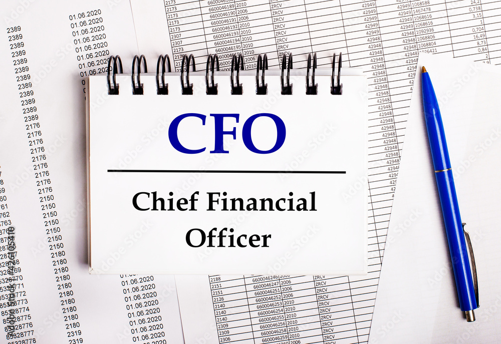 On the table are charts and reports, on which lie a blue pen and a notebook with the word CFO Chief Financial Officer On the table are charts and reports, on which lie a blue pen and a notebook with the word CFO Chief Financial Officer