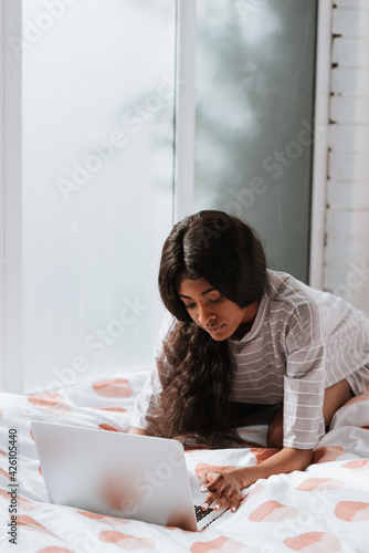 Beautiful young African female with long hair using a laptop computer in bed photo