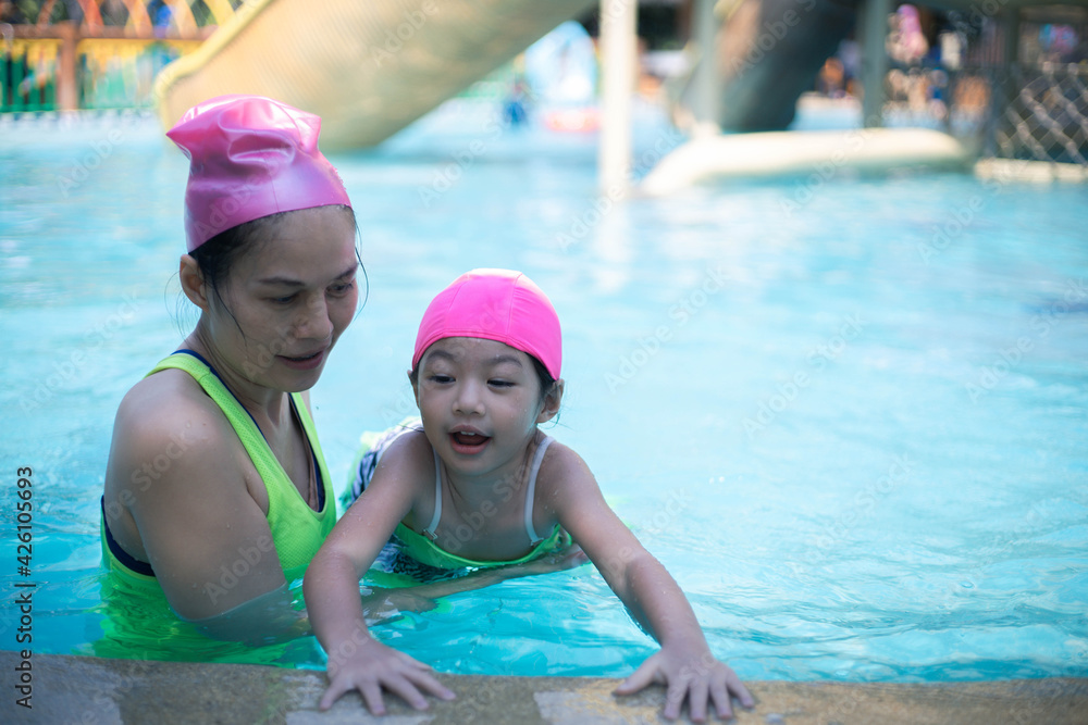 Asian mother and daughter in swimming pool, aquapark. Sunny summer.