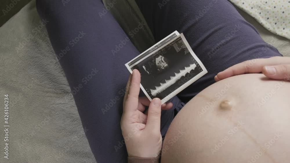 expecting pregnant woman with large belly looking at ultrasound scan at home expecting pregnant woman with large belly looking at ultrasound scan at home