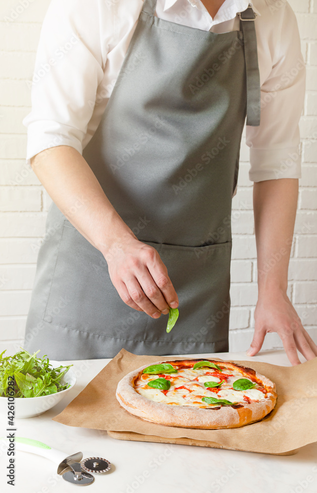 chef puts green basil leaves on the pizza