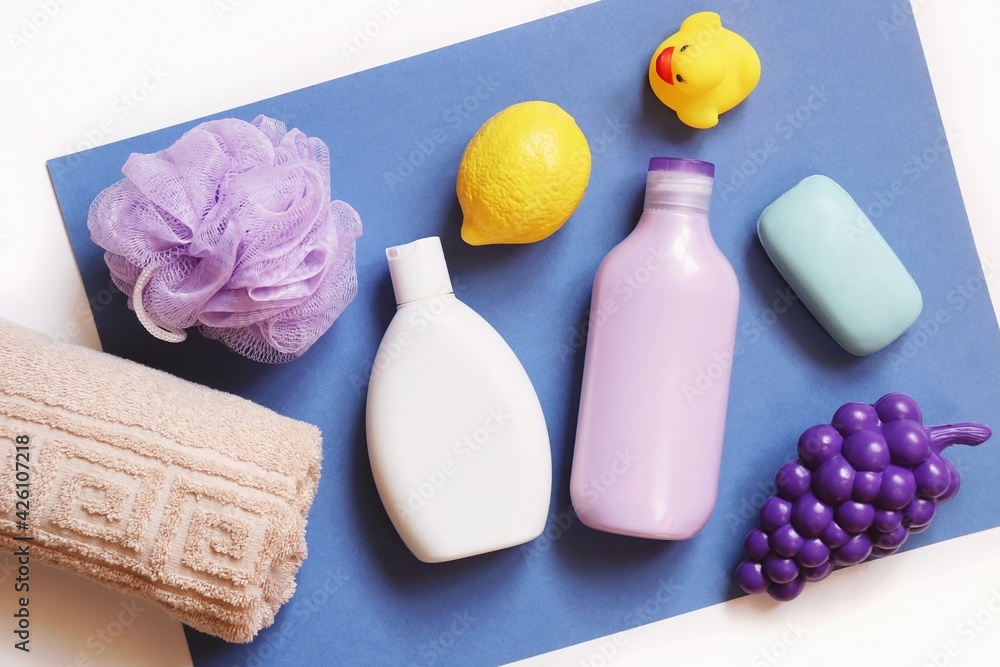 Flat lay natural organic bath products, baby care cosmetics set. Beige towel, purple sponge, shampoo bottle, shower gel, soap bar and toys on a blue background Flat lay natural organic bath products, baby care cosmetics set. Beige towel, purple sponge, shampoo bottle, shower gel, soap bar and toys on a blue background