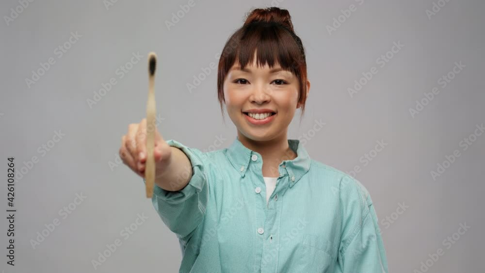 dental care, oral hygiene and people concept - portrait of happy smiling young asian woman in turquoise shirt with wooden toothbrush over grey background