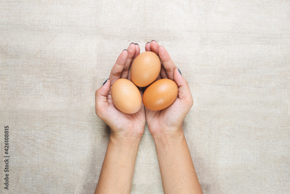 Top view of Young woman's hands, holding eggs in the hands on sack background. Selective focus. Care or attentive concept.