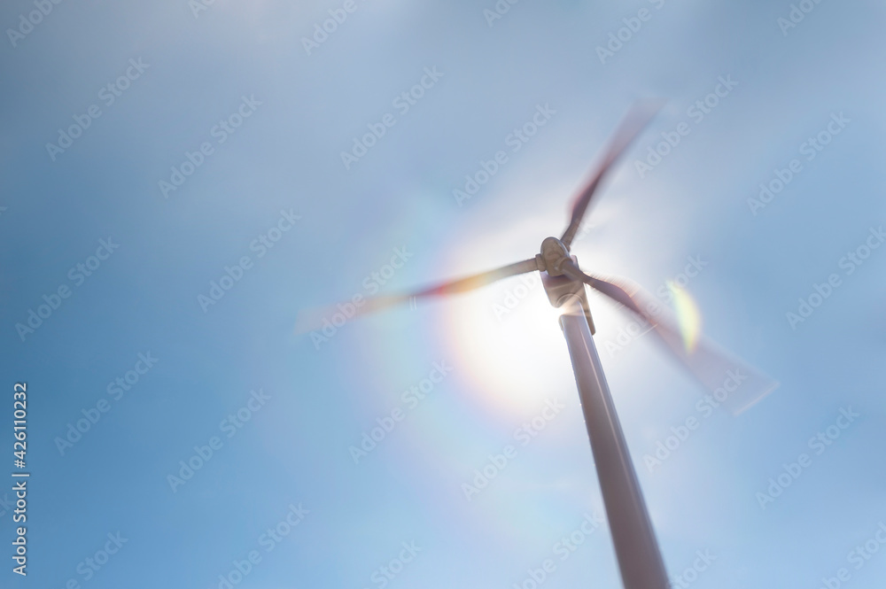 Low angle view of wind turbine against blue sky and sun Low angle view of wind turbine against blue sky and sun