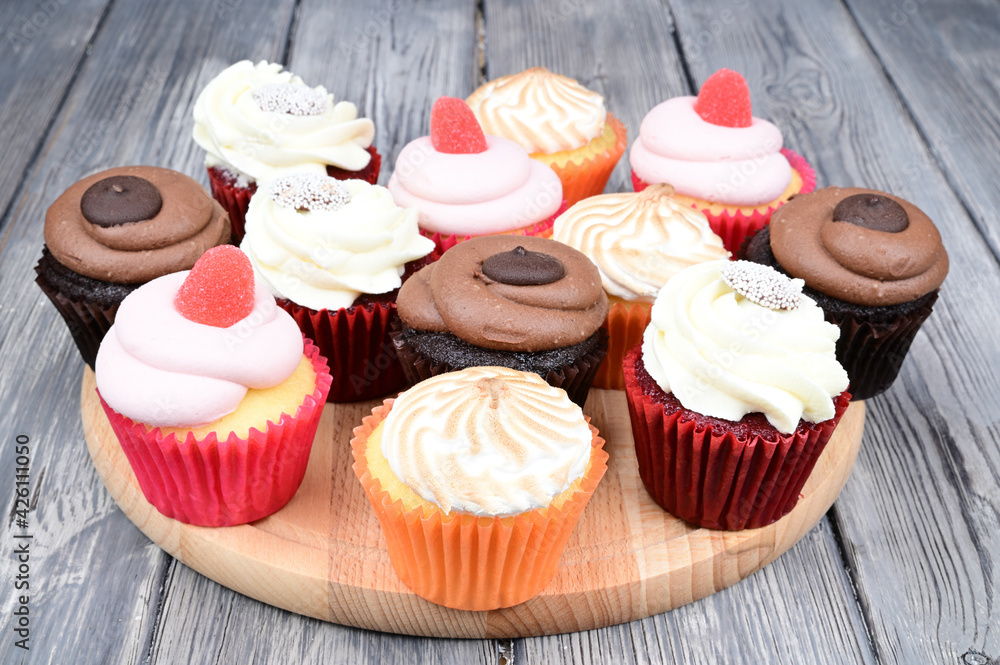 Side view of several multi-colored cupcakes laid out on a wooden cutting board