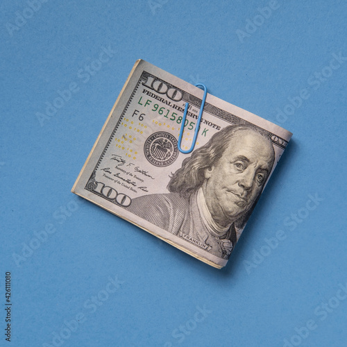 Folded one hundred dollar bill with paper clip on blue background
