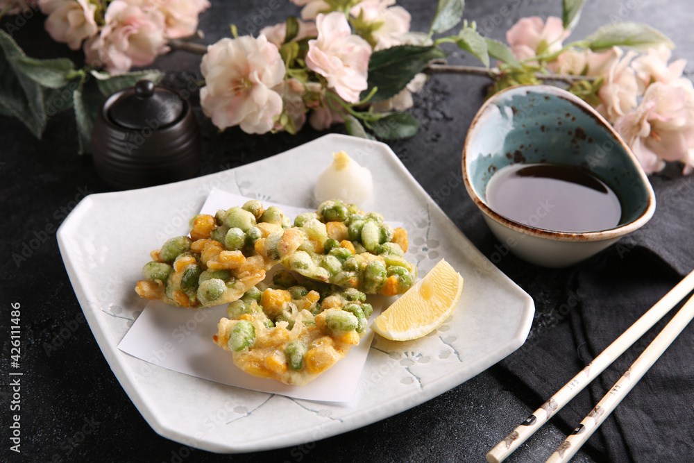 Japanese cuisine. Vegetables, green peas in tempura on a white plate on a black table with soy sauce. Restaurant menu. Background image, copy space