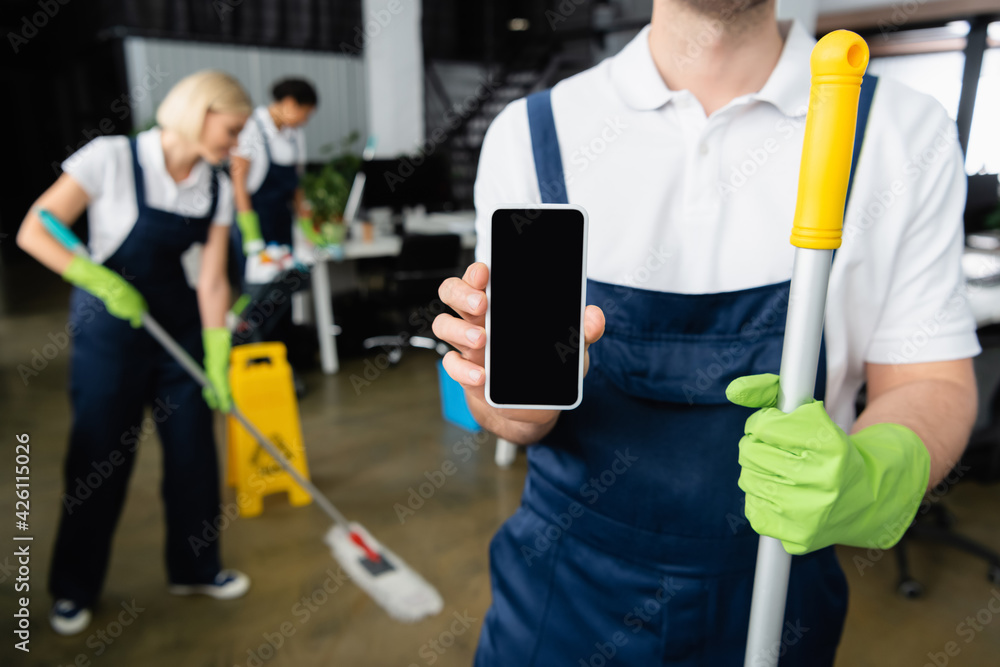 Cleaner holding smartphone and mop in office Cleaner holding smartphone and mop in office