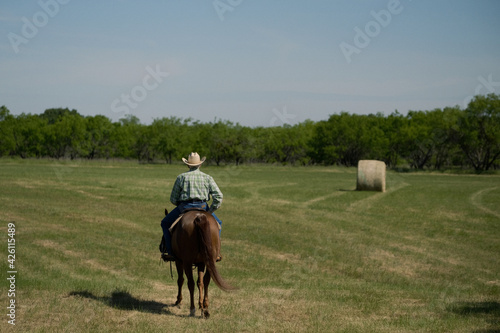 Western lifestyle shows cowboy riding horse through rural Texas landscape during summer on ranch.