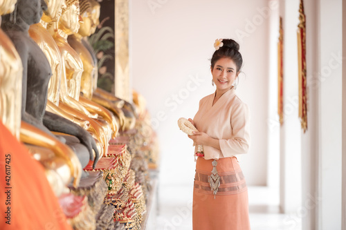 Thai beautiful women in traditional Thai dress use fresh flower garlands to pay homage to the Buddha image, To make a wish on the Thai Songkran Festival © ritfuse