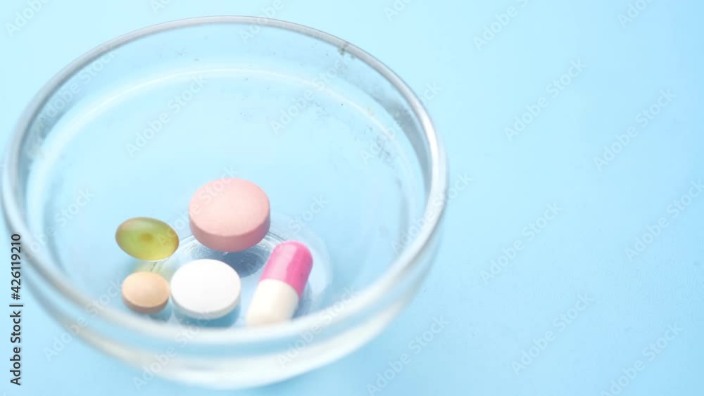 Close up of medical pills and capsules in a small container on blue background Close up of medical pills and capsules in a small container on blue background
