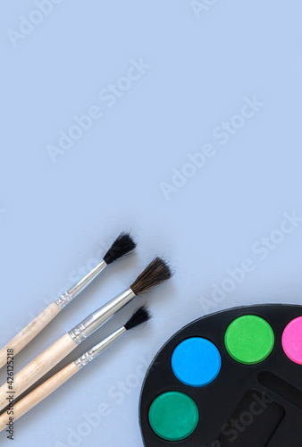 Art palette with paint and paintbrushes top view on gray background