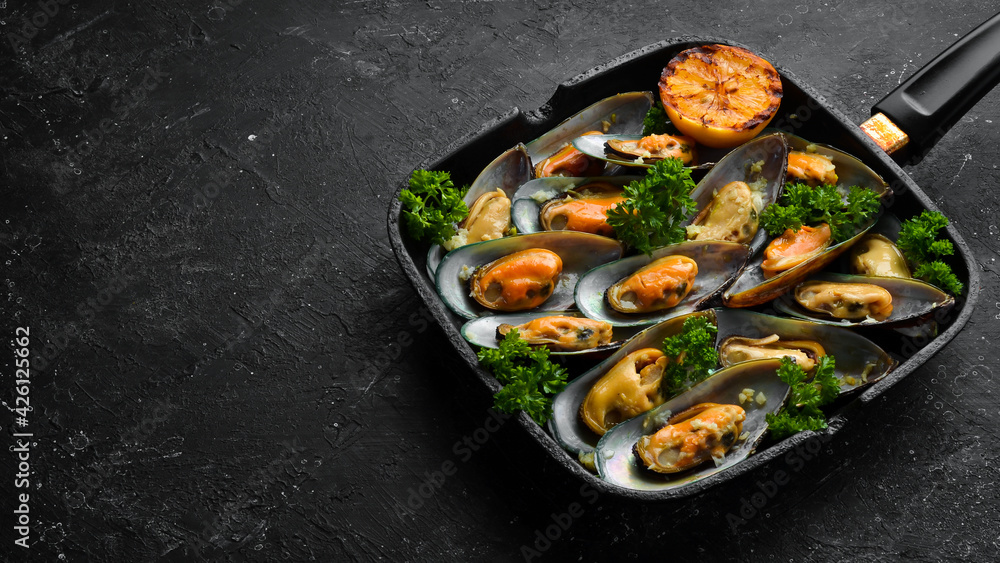 Frying pan with fried mussels with garlic, parsley, lemon and spices. On a black stone background. Free space for text. Frying pan with fried mussels with garlic, parsley, lemon and spices. On a black stone background. Free space for text.