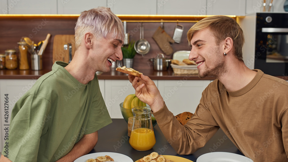 Smiling young caucasian gay couple eating toast