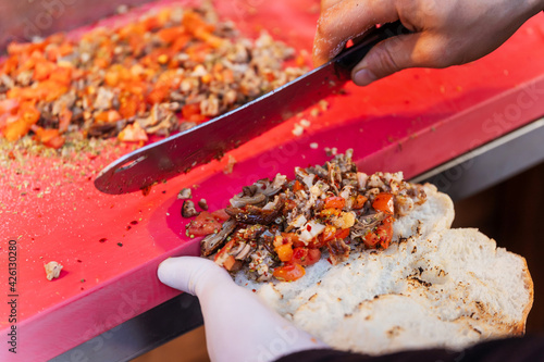 Slicing the filling for traditional Turkish fast food Kokorech. Bread loaf with roasted lamb intestines in Istanbul. The knife and the hand of the cook prepares the filling for the kokorech photo