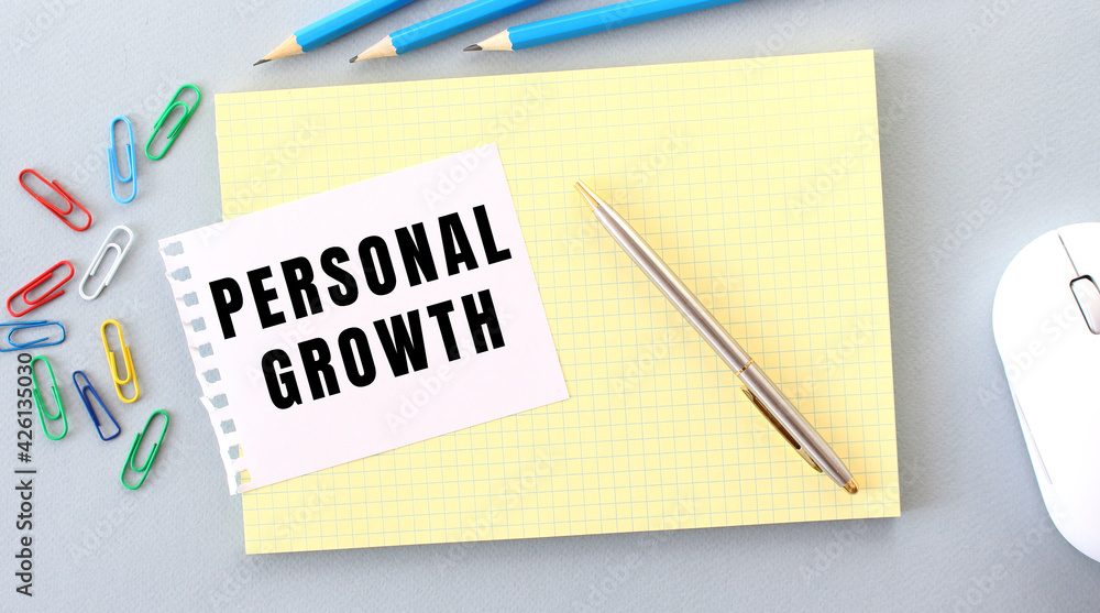 PERSONAL GROWTH is written on a piece of paper that lies on a notebook next to office supplies. PERSONAL GROWTH is written on a piece of paper that lies on a notebook next to office supplies.