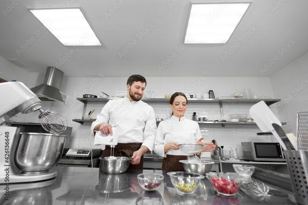 Pastry chef a man and a woman in a professional kitchen prepare a sponge cake, mix the ingredients and sift the flour.