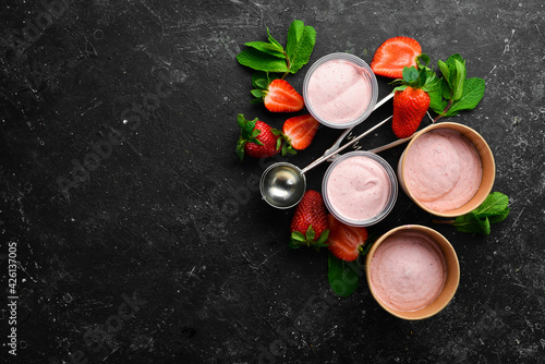 Strawberry ice cream with mint and strawberries. Ice cream spoon. On a black stone background, top view.