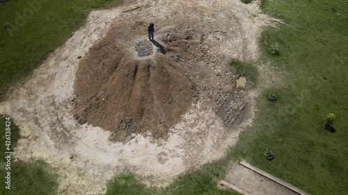 Epic aerial of an East Indian woman standing on a cone shaped mud volcano located in Penal, Trinidad photo