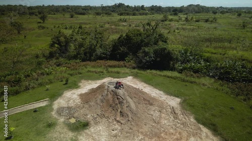 A couple sits atop a cone shaped mud volcano aerial 360 pan view photo