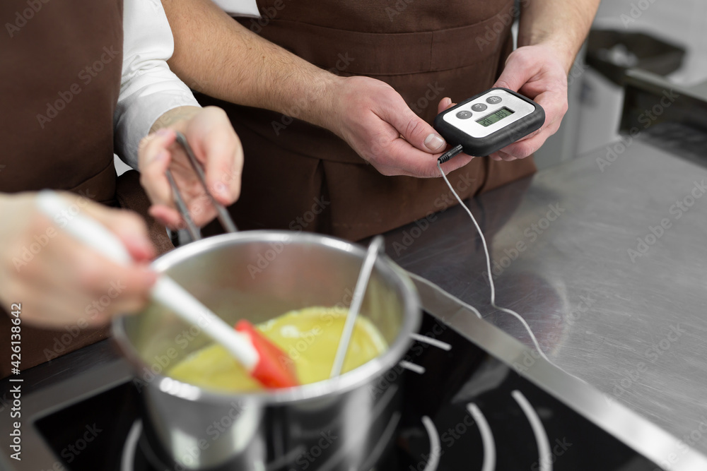Close-up of the hands of a man and a woman-confectioners, who together prepare a dessert in a professional kitchen, cook syrup and measure its temperature.