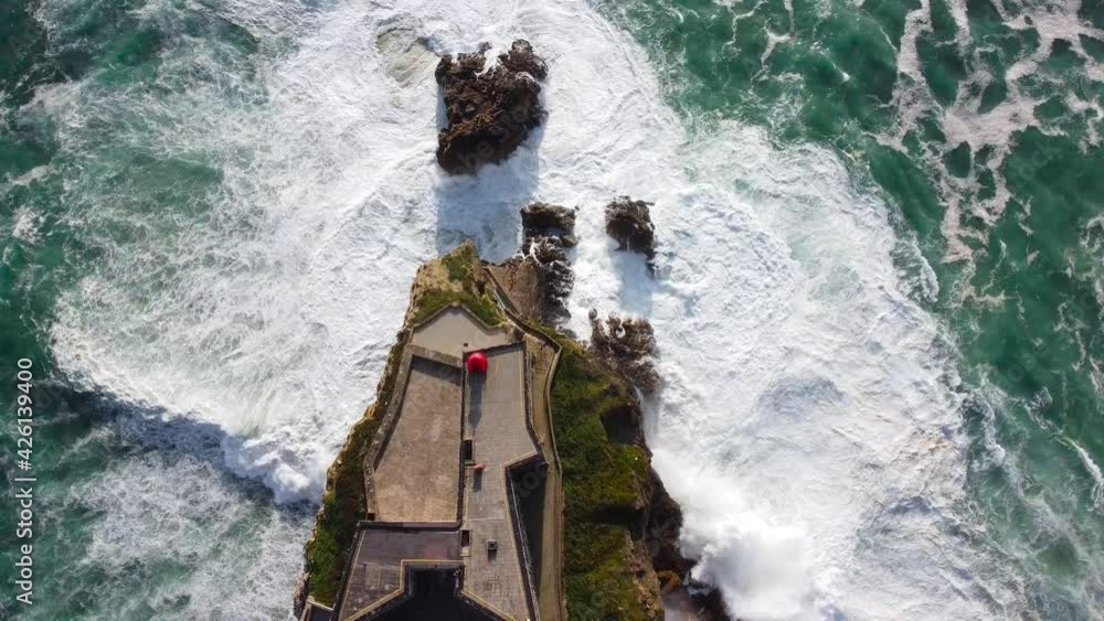 4k aerial slow motion, top down, close up view of lighthouse in Nazare. In front of the big,powerfull waves.Blue turquoise colors