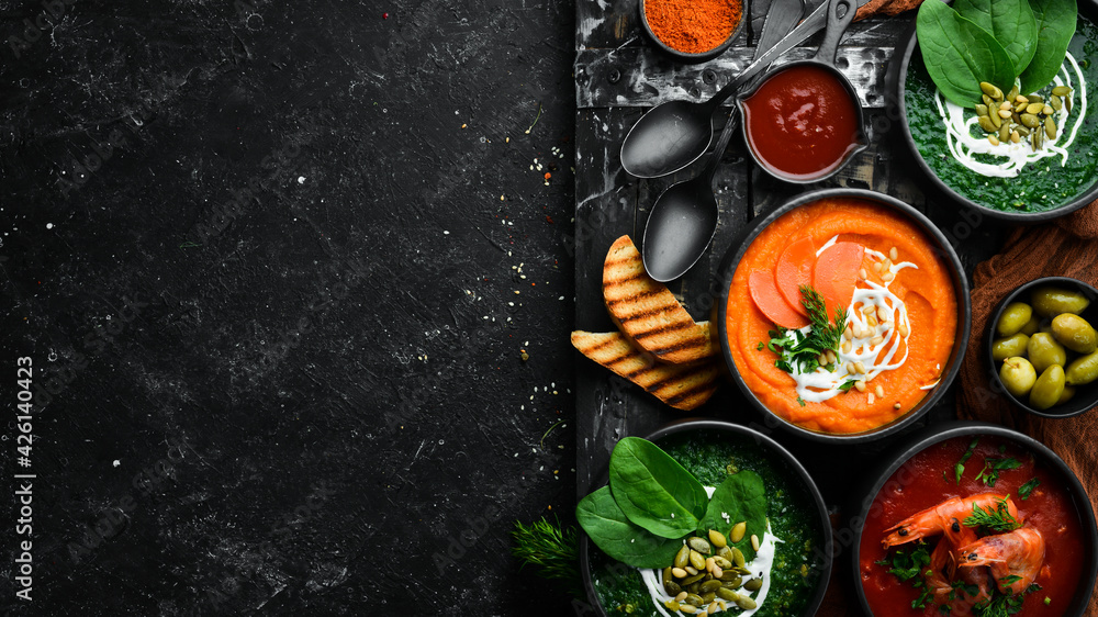 Set of colored soups. Spinach soup, tomato cream soup and carrot puree soup. Healthy food. On a black stone background.