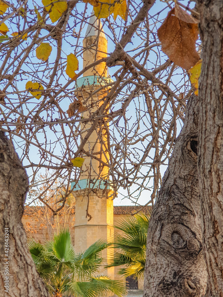 View of Omeriye Mosque minaret in Nicosia, Cyprus, through tree leaves and branches in a beautiful sunny afternoon. View of Omeriye Mosque minaret in Nicosia, Cyprus, through tree leaves and branches in a beautiful sunny afternoon.
