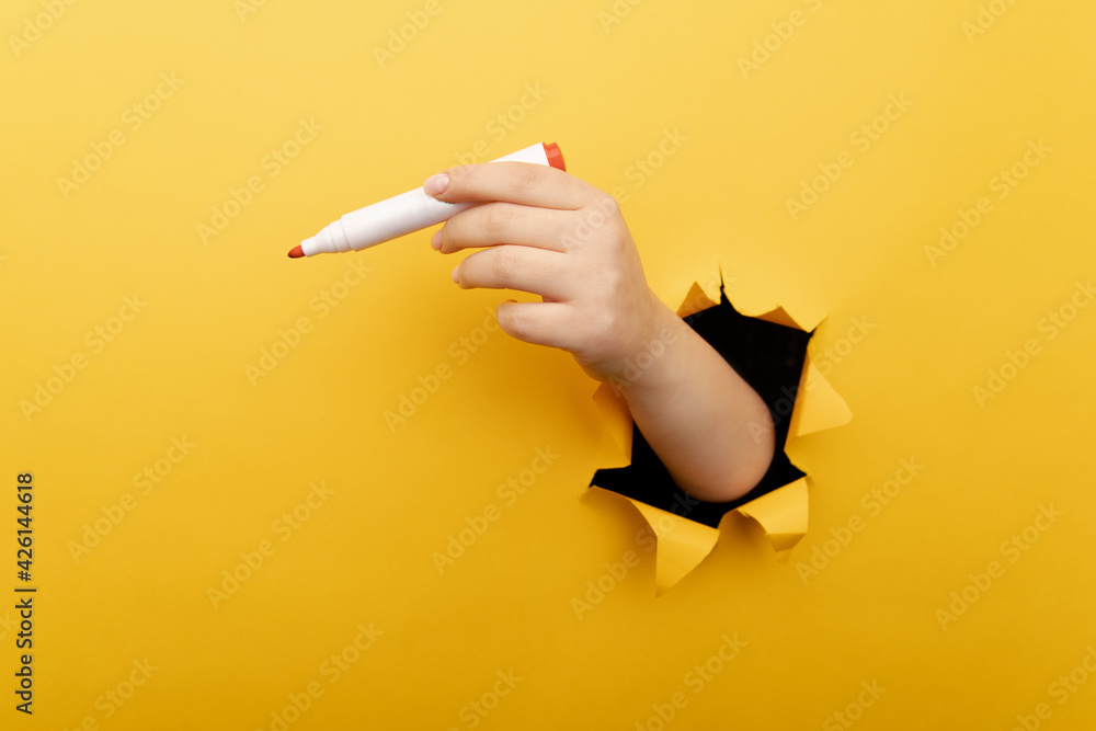A hand with marker though a broken yellow paper wall. - obrazy, fototapety, plakaty 