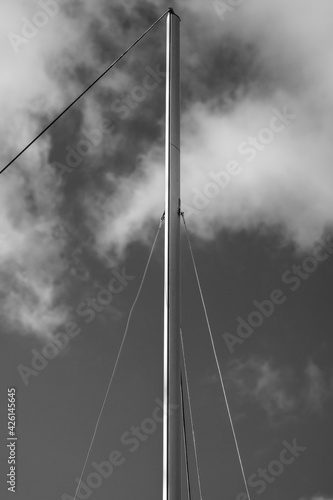 The mast of a boat in front of a cloudy sky in black and white.