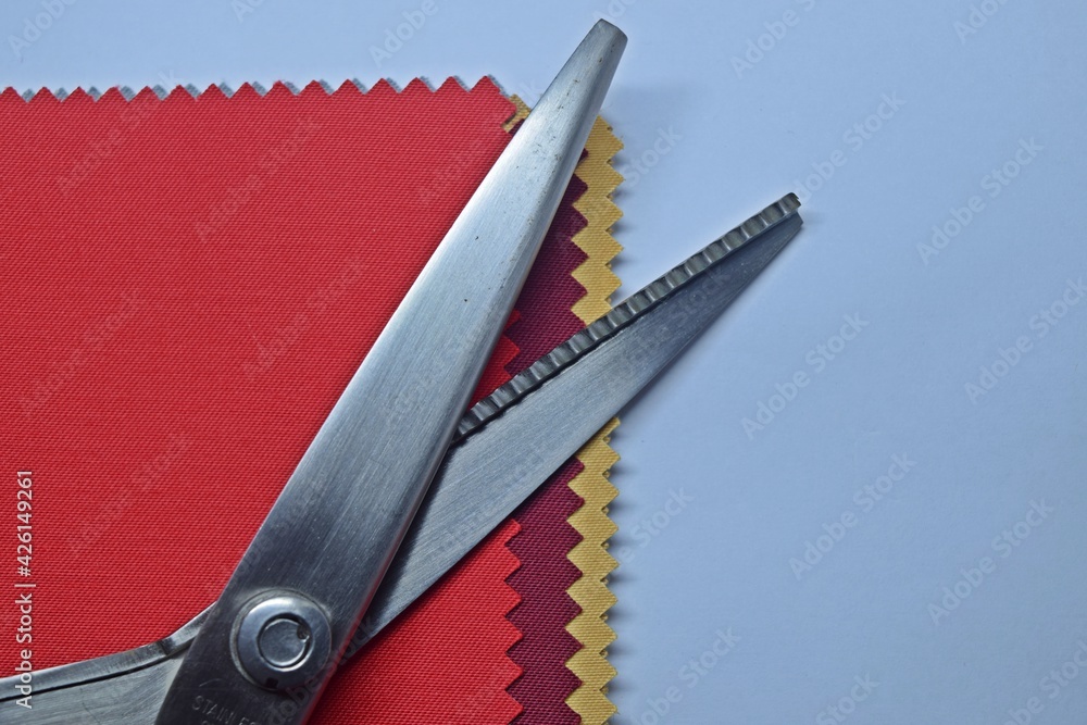 Zig Zag Scissors and examples of cloth pieces of red, dark red, gold on  white background. Stock Photo