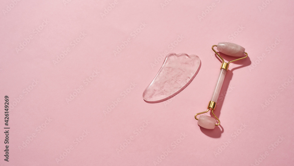 Rose quartz facial massage tools, face roller and Gua Sha scraper isolated over pink background Rose quartz facial massage tools, face roller and Gua Sha scraper isolated over pink background