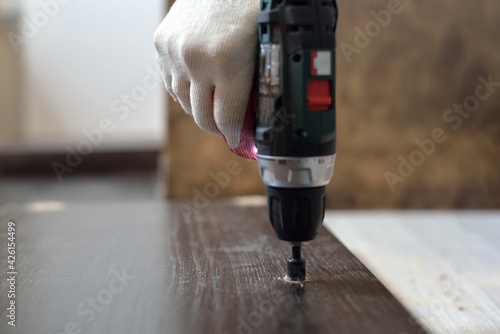 In purple, a man drills a hole in a blank for laminating MDF furniture. MDF furniture assembly concept