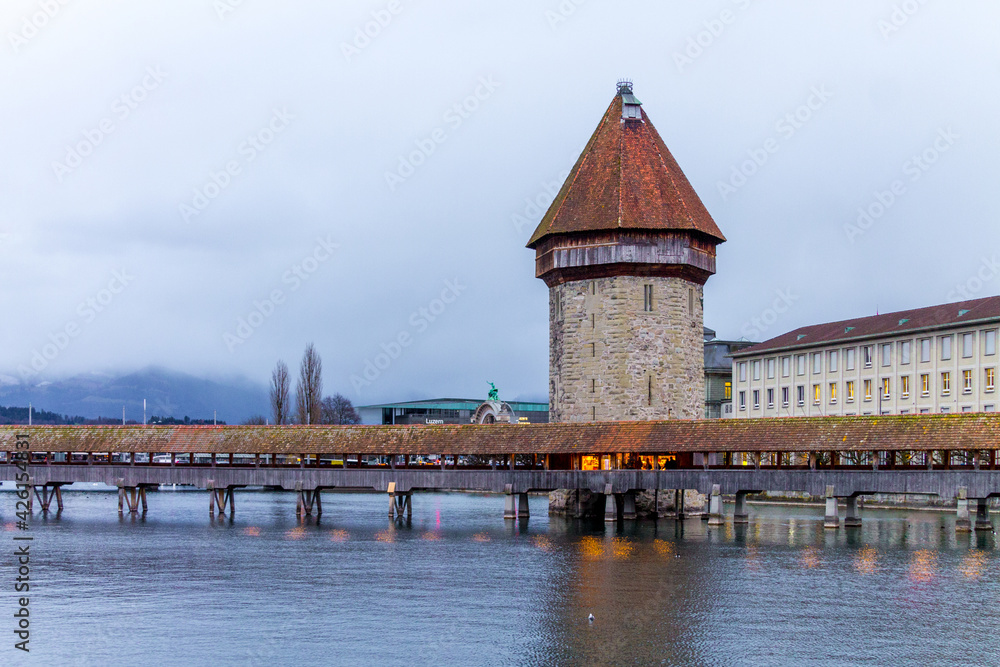 View of wooden bridge and famous chapel in Lucerne lake on cloudy winter day, Switzerland.