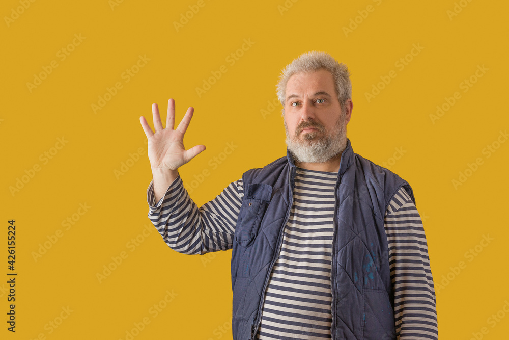 A man with a gray beard shows hand with fingers splayed. On a yellow isolated background. A man with a gray beard shows hand with fingers splayed. On a yellow isolated background.