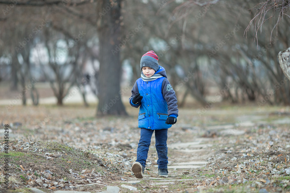 A Caucasian six-year-old boy in blue clothes walks in the park