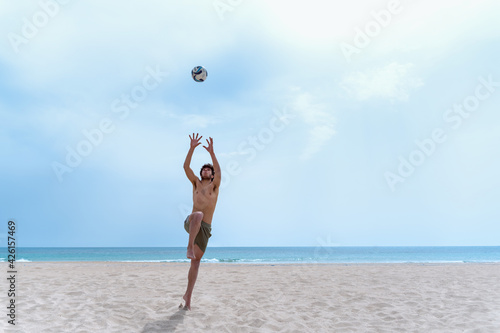 Shirtless young man on the beach jumps to catch a ball.