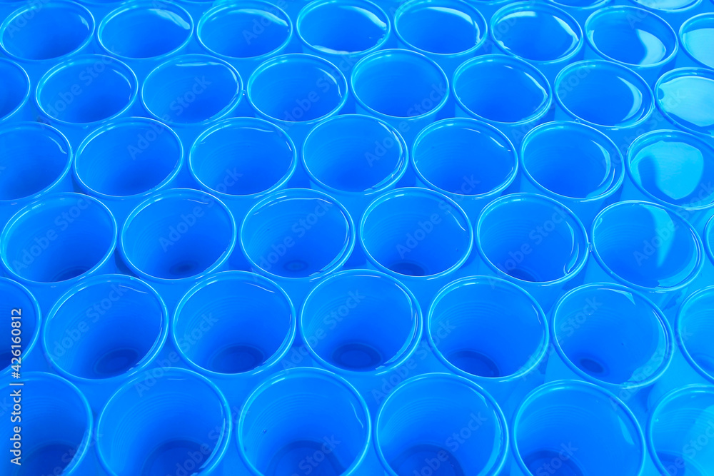 Clear water in blue plastic disposable cups. Abstract background.