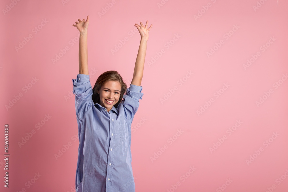 a happy young girl in a blue shirt with her hands up in the air on a pink background. the concept of joy and fun a happy young girl in a blue shirt with her hands up in the air on a pink background. the concept of joy and fun