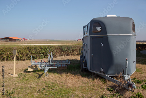 silver horse trailer on green weadow . A trailer used for transporting one adult horse A trailer used for transporting one adult horse. A horse trailer with graphics is ready to hook up and go . photo